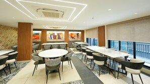 A modern dining area with round tables and chairs, a patterned floor, and a view of the city through large windows. - ALIVAA boutique DLF Cybercity Gurugram (Gurugram)