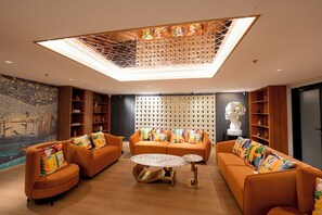Un salon moderne avec des canapés orange, une table basse en marbre et un plafond doté d’une verrière.