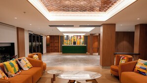 A lobby with a reception desk, orange sofas, a marble coffee table, and a geometric ceiling design. - ALIVAA boutique DLF Cybercity Gurugram (Gurugram)