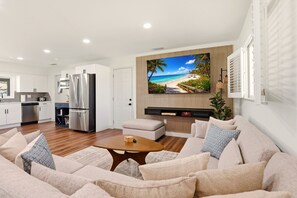 A modern living room with a beige sofa, a wooden coffee table, and a large flat-screen TV mounted on a wall above a wooden panel. - New! 10 mins to beach, Family Resort, Heated Pool, Mini-golf, Pickleball (Bradenton)
