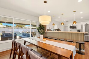 A modern kitchen with a central island, bar stools, and a dining area with a long table and chairs. - New! 10 mins to beach, Family Resort, Heated Pool, Mini-golf, Pickleball (Bradenton)