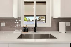 Una cocina moderna con un lavamanos de acero inoxidable, una ventana sobre el lavamanos y vistas al exterior.
