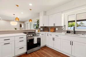 A modern kitchen with white cabinetry, a stainless steel stove, and a large window. - New! 10 mins to beach, Family Resort, Heated Pool, Mini-golf, Pickleball (Bradenton)