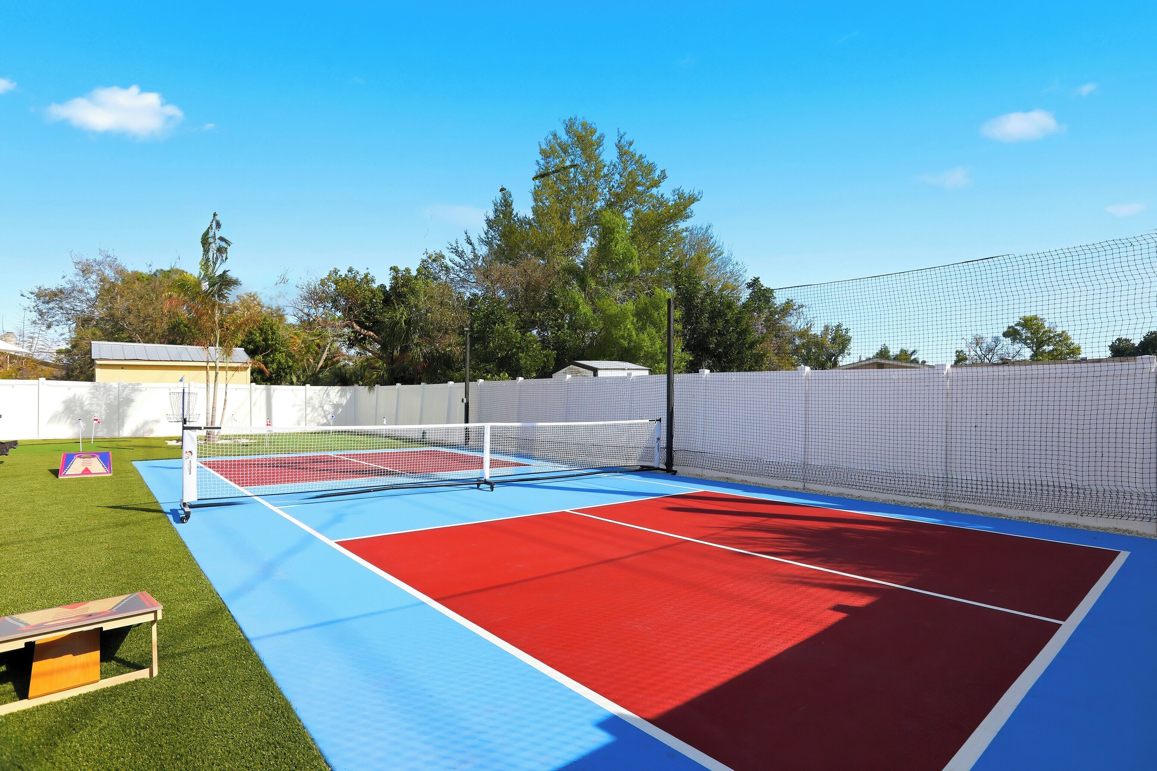 An outdoor tennis court with a net, green artificial turf, and a red and blue playing surface.