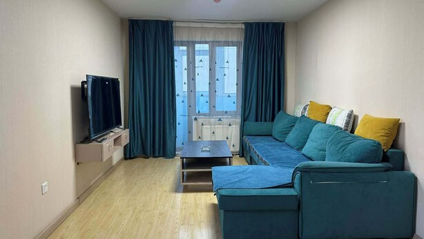 Ein gemütlicher Wohnraum mit einer Couch, einem Fernseher und einem Fenster mit Vorhängen.
