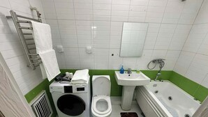 Ein kleines, sauberes Badezimmer mit Waschmaschine, Toilette, Waschbecken und Badewanne.