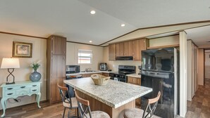 A kitchen with a central island, bar stools, wooden cabinets, a refrigerator, and a microwave. - 2 Mi to Ocean! Family-Friendly Emerald Coast Haven (Fort Walton Beach)
