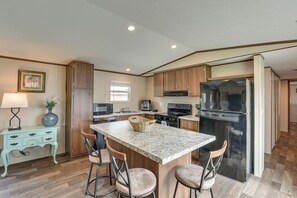 A kitchen with a central island, bar stools, wooden cabinets, a refrigerator, and a microwave. - 2 Mi to Ocean! Family-Friendly Emerald Coast Haven (Fort Walton Beach)