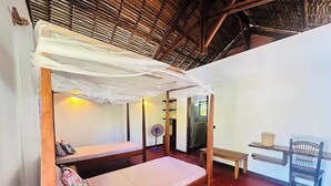 Ein Zimmer mit einem Bett, einer Bank, einem Stuhl, einem Ventilator und einem Tisch.