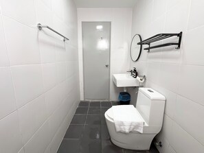 A bathroom with white tiles, a toilet, a sink, a mirror, and a shower area. - Aurora Residence by Manhattan Group (Puchong)