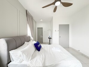 A modern hotel room with a large bed, a ceiling fan, a door, and a small ironing station. - Aurora Residence by Manhattan Group (Puchong)