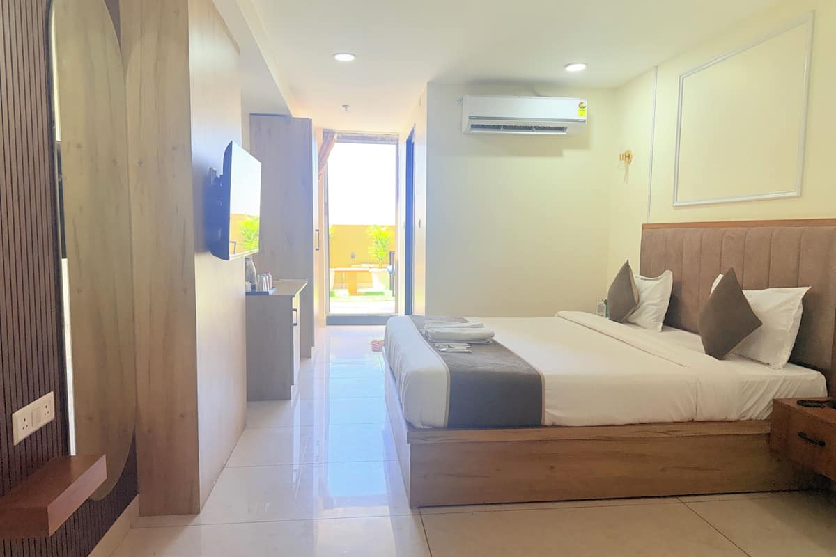 A hotel room with a bed, a desk, a TV, and an air conditioning unit.