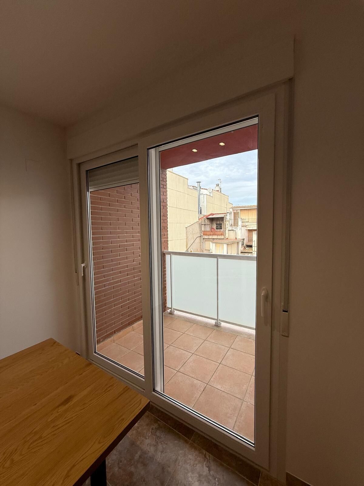A room with a sliding glass door leading to a balcony with a tiled floor and a view of buildings.