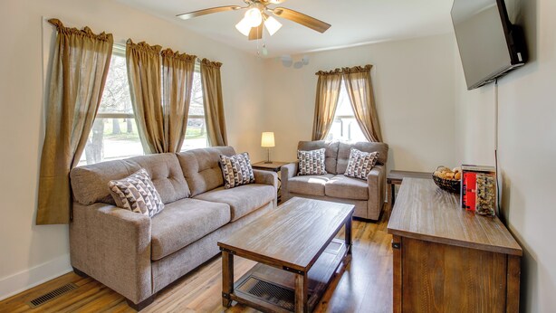 A living room with two sofas, a coffee table, a ceiling fan, a flat-screen TV, and a window with curtains. - Lakes, Whiskey & More! Charming Home in Tullahoma (Tullahoma)