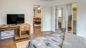 Ein Schlafzimmer mit Bett, Schreibtisch mit Fernseher, Kleiderschrank und einer Tür zu einem anderen Raum.