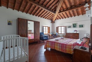 A bedroom with a wooden ceiling, a crib, a bed with a plaid bedspread, a desk, and a chair. - Flat With Swimming Pool and air Conditioning (Peccioli)