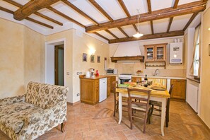 Una cucina accogliente con travi in legno, un tavolo da pranzo con sedie, un divano floreale e un piccolo frigorifero.
