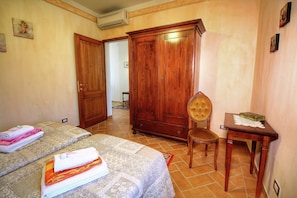 Ein Schlafzimmer mit zwei Betten, einem Holzschrank, einem Stuhl und einem kleinen Tisch mit einem Buch.