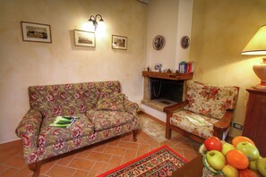 Un soggiorno con un divano floreale, una poltrona in legno, un camino e una ciotola di frutta su un tavolo.