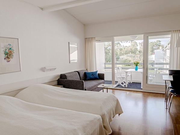 Ein Hotelzimmer mit zwei Betten, einem Sofa, einem Tisch und einem Balkon mit Blick.