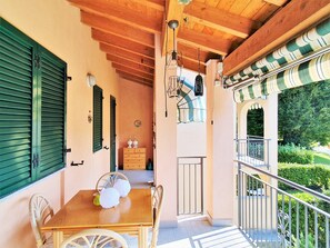 A wooden balcony with a table and chairs, a small cabinet, and a view of greenery. - Belvilla by OYO Bos03/3 (Montegrino Valtravaglia)