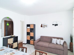Ein Wohnzimmer mit einer Couch, einem Esstisch mit Stühlen, einem Bücherregal und einer Heizung.