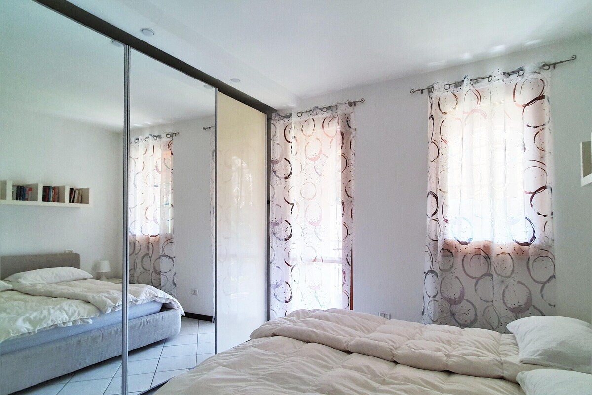 Ein Schlafzimmer mit einem Bett, einem Kleiderschrank, einem Spiegel und Vorhängen.