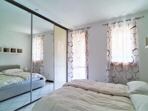 A bedroom with a bed, a wardrobe, a mirror, and curtains. - Belvilla by OYO Bos03/3 (Montegrino Valtravaglia)