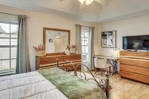 Ein Schlafzimmer mit einem Bett, einem Schreibtisch, einem Stuhl, einer Kommode, einem Fernseher und einem Fenster mit Vorhängen.