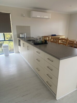 A modern kitchen with a built-in oven, a sink, and a dining area with wooden chairs.