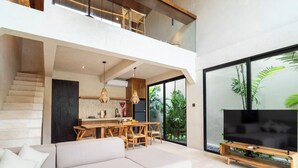 Ein zeitgemäßer Wohnraum mit Treppe, Essbereich, Sofa, Fernseher und großen Fenstern mit Pflanzen.