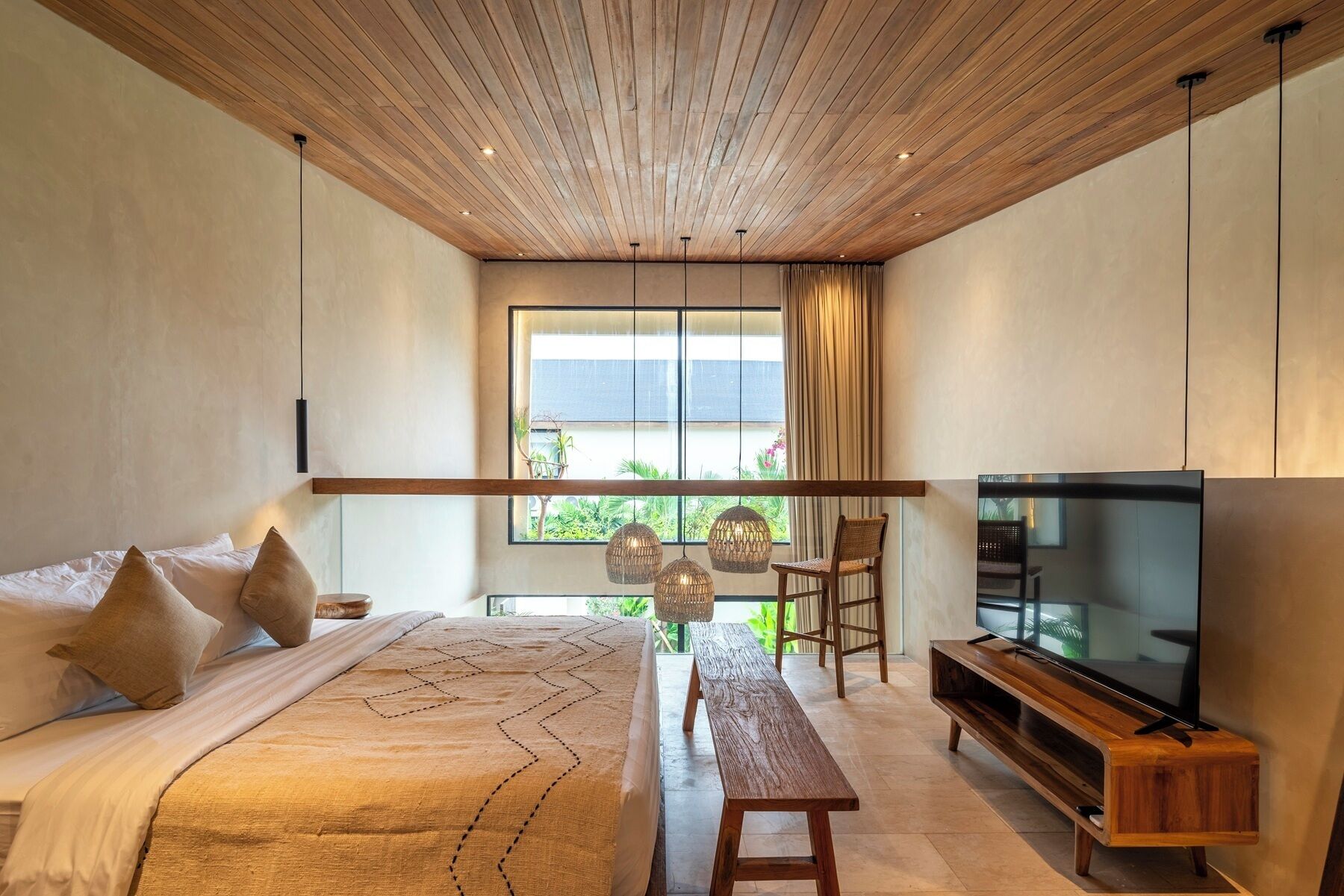 Een slaapkamer met een bed, een bankje, een televisie en een raam met uitzicht.