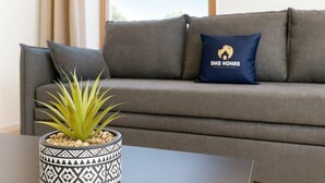 Una sala moderna con un sofá gris, un cojín decorativo y una planta en maceta sobre una mesa.