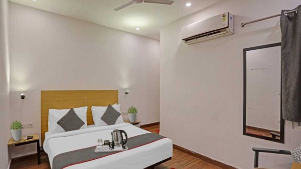 A neatly arranged hotel room with a bed, a small table, a chair, a red rug, an air conditioning unit, and a ceiling fan. - Townhouse Samaypur Badli Metro Station (New Delhi)