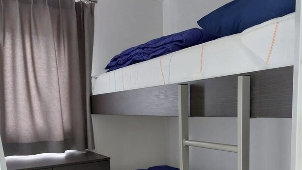 Una cama litera con ropa de cama azul, un escritorio pequeño y un armario.