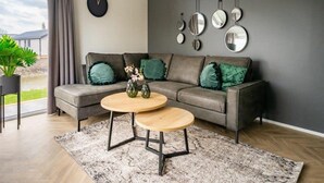 Una sala de estar moderna con un sofá gris, una mesa de centro redonda de madera y un amplio ventanal con cortinas.