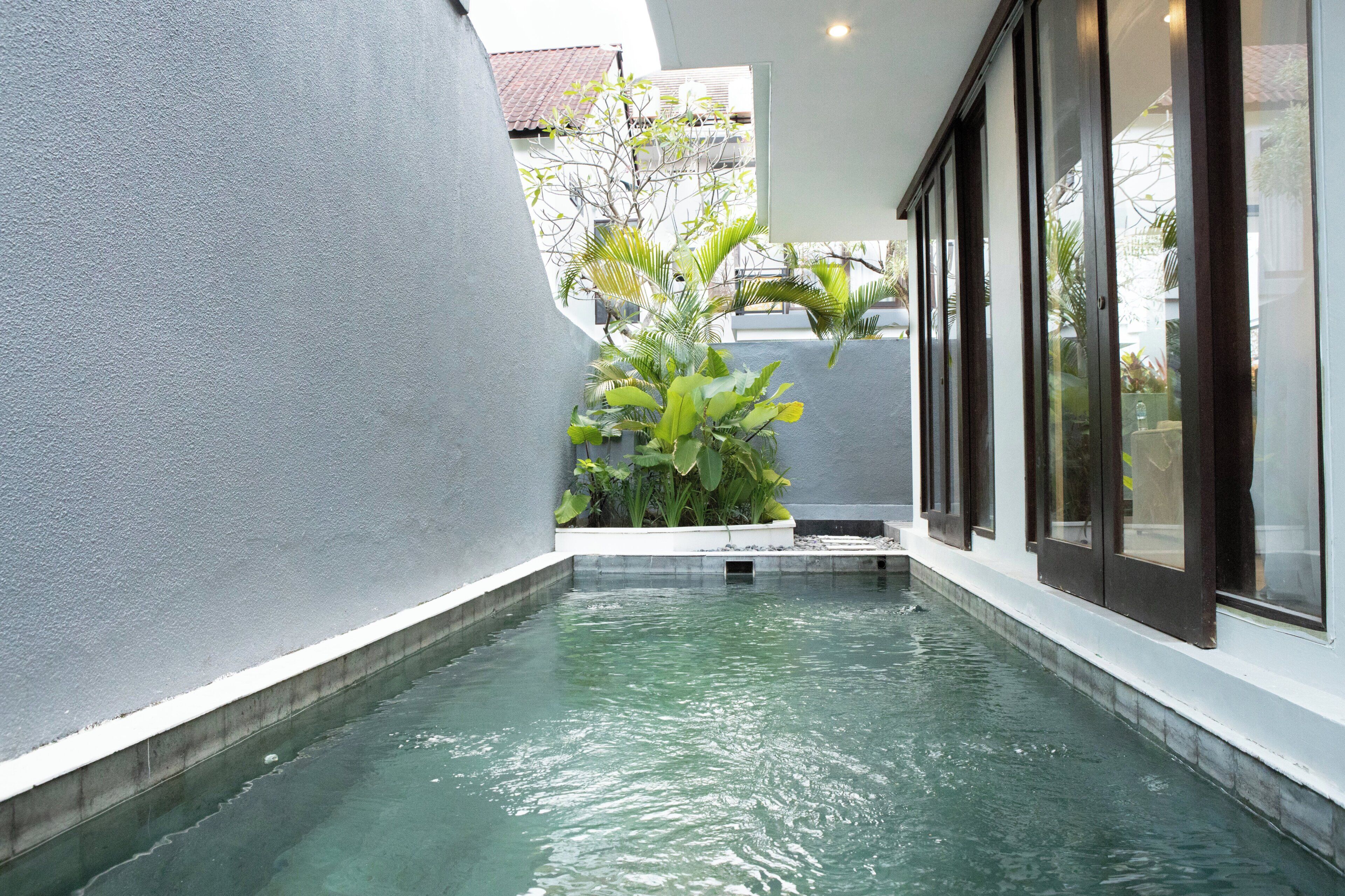 A narrow water feature with a concrete border, surrounded by a building with large windows and a white exterior.