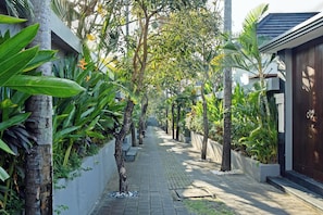 A pathway lined with trees and plants, leading to a building with a dark door. - Grand Kesambi Villa (Kerobokan)