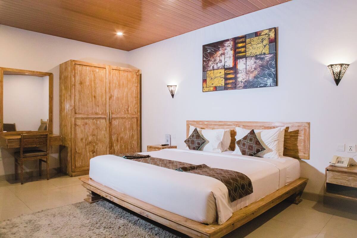 Une chambre avec un grand lit, une armoire en bois, un bureau et une chaise, ainsi qu’une œuvre d’art accrochée au mur.