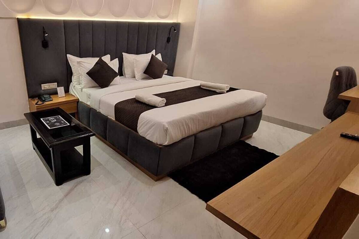 A modern hotel room with a bed, a sofa, a nightstand, and a wooden desk.