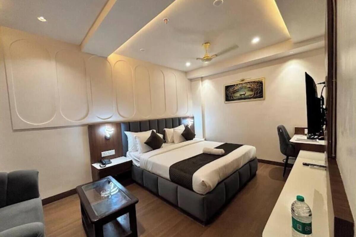 A modern hotel room with a large bed, a desk, a chair, a small table, and a ceiling fan.