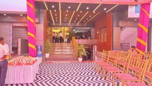 Een hotel lobby met een receptiebalie, een trap die naar de bovenverdieping leidt, en rijen stoelen gerangschikt voor een vergadering of evenement.