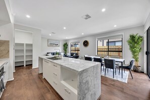 Una cocina moderna con una isla de mármol, armarios blancos y una zona de comedor con mesa y sillas.