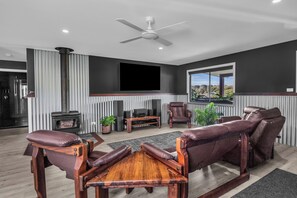 Ein modernes Wohnzimmer mit Kamin, Ledersessel, Couchtisch aus Holz und Deckenventilator.