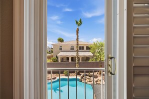 A view through a door with a pool, a palm tree, and a house in the background. - Vegas Grand Villa - 5BR, Pool, Putting Green (Las Vegas)