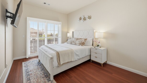 A bedroom with a bed, nightstands, a lamp, a wall-mounted TV, and a view through the window. - Vegas Grand Villa - 5BR, Pool, Putting Green (Las Vegas)