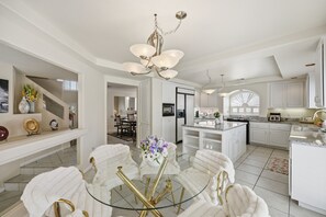 A spacious kitchen with white cabinetry, a central island, and a dining area with a glass table and white chairs. - Vegas Grand Villa - 5BR, Pool, Putting Green (Las Vegas)