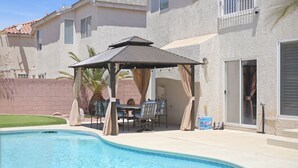 A swimming pool with a covered patio area, a brick wall, and a building with windows and a door. - Vegas Grand Villa - 5BR, Pool, Putting Green (Las Vegas)