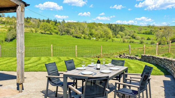 An outdoor dining area with a table set for four, surrounded by chairs, overlooking a green landscape with a stone wall and a wooden structure. - 3 bedroom accommodation in Brough (Brough)