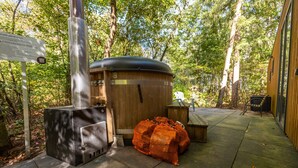 A wooden outdoor structure with a metal grill and a large orange bag, surrounded by trees. - Drenthe Wellness Lodge for 4 (Ruinen)